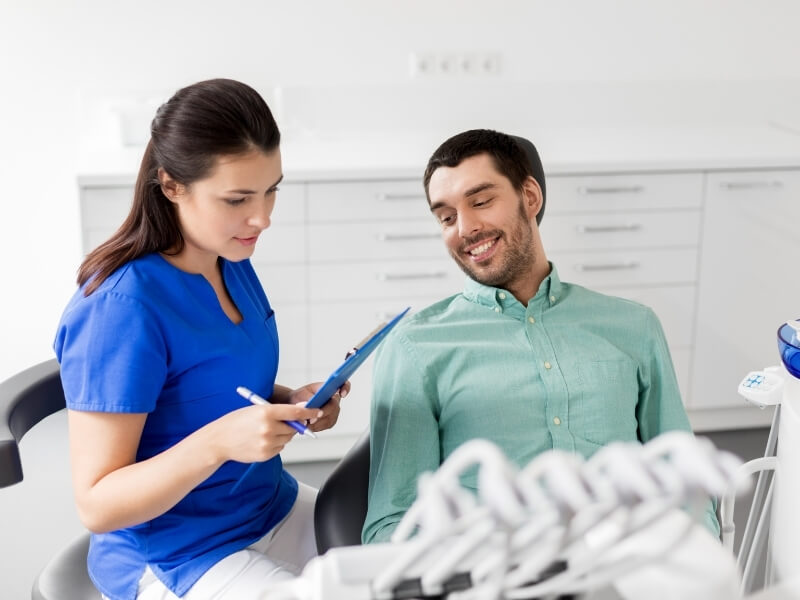 Smiling male patient sitting in a dental chair reviewing notes with a female dental assistant