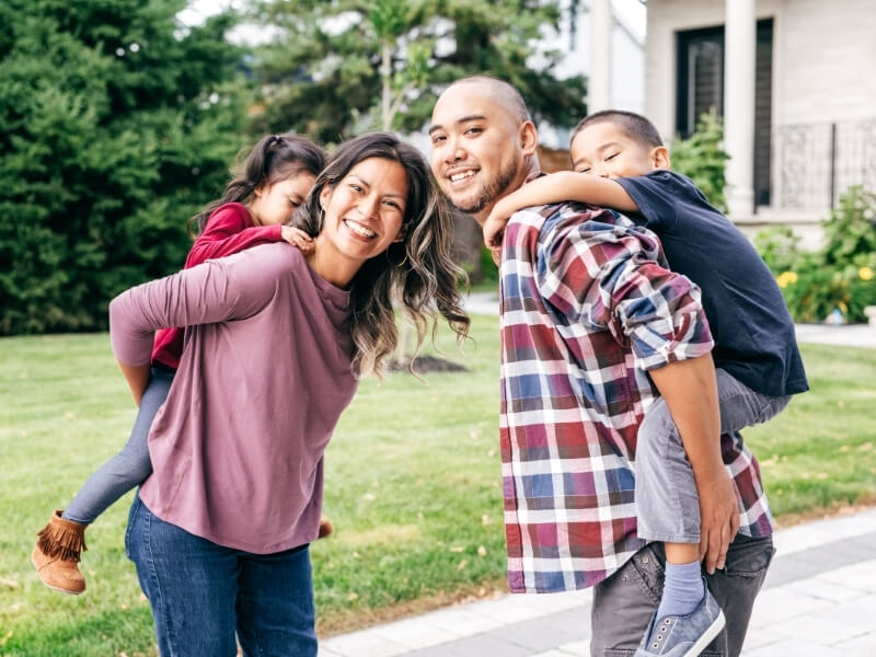 Smiling family with mother and father both carrying elementary school aged children on their backs