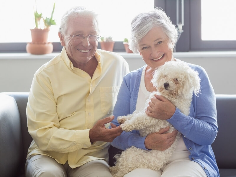 Smiling retired couple sitting on a couch while holding a lapdog