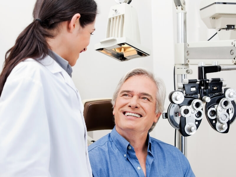 Older male patient smiling while looking up at his eye doctor